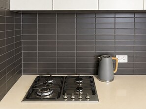 A kitchen with two gas stoves, a kettle, and a power outlet on the countertop. - Stylish Modern Studio - A Sweet Escape for Two (Box Hill)