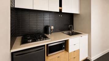 A modern kitchen with a black tiled backsplash, a stainless steel sink, a black kettle, and a built-in dishwasher.