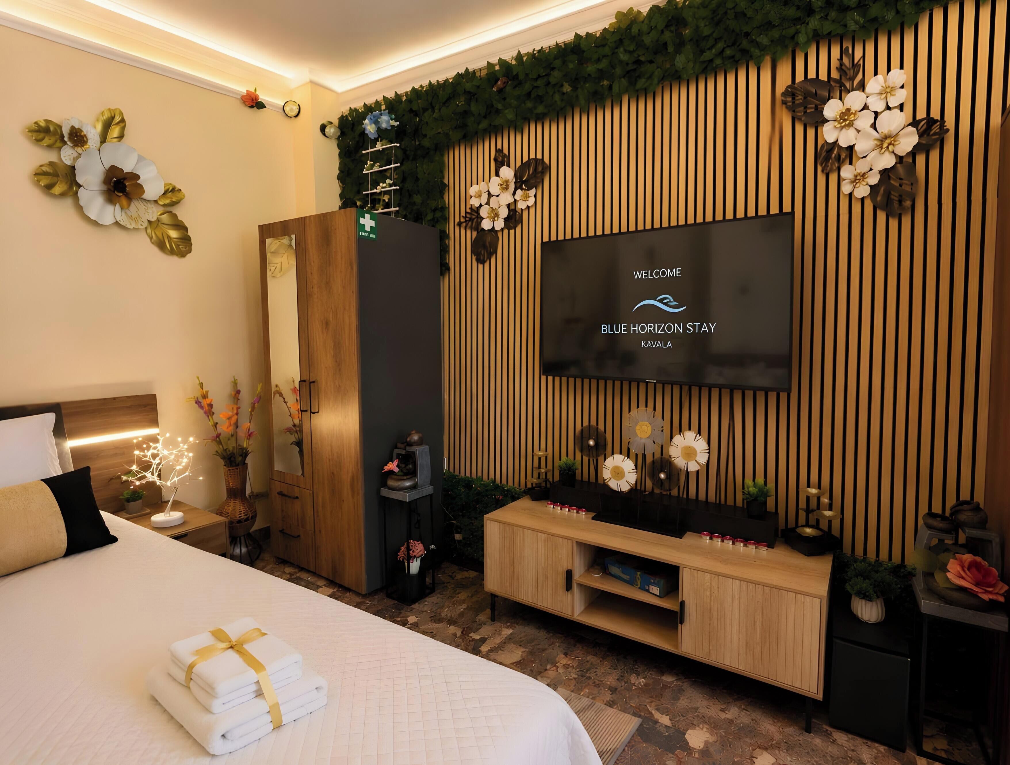Una camera d'albergo con un letto, una TV a parete, un mobiletto in legno e un tavolino con un vaso di fiori.