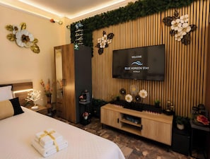 Una camera d'albergo con un letto, una TV a parete, un mobiletto in legno e un tavolino con un vaso di fiori.