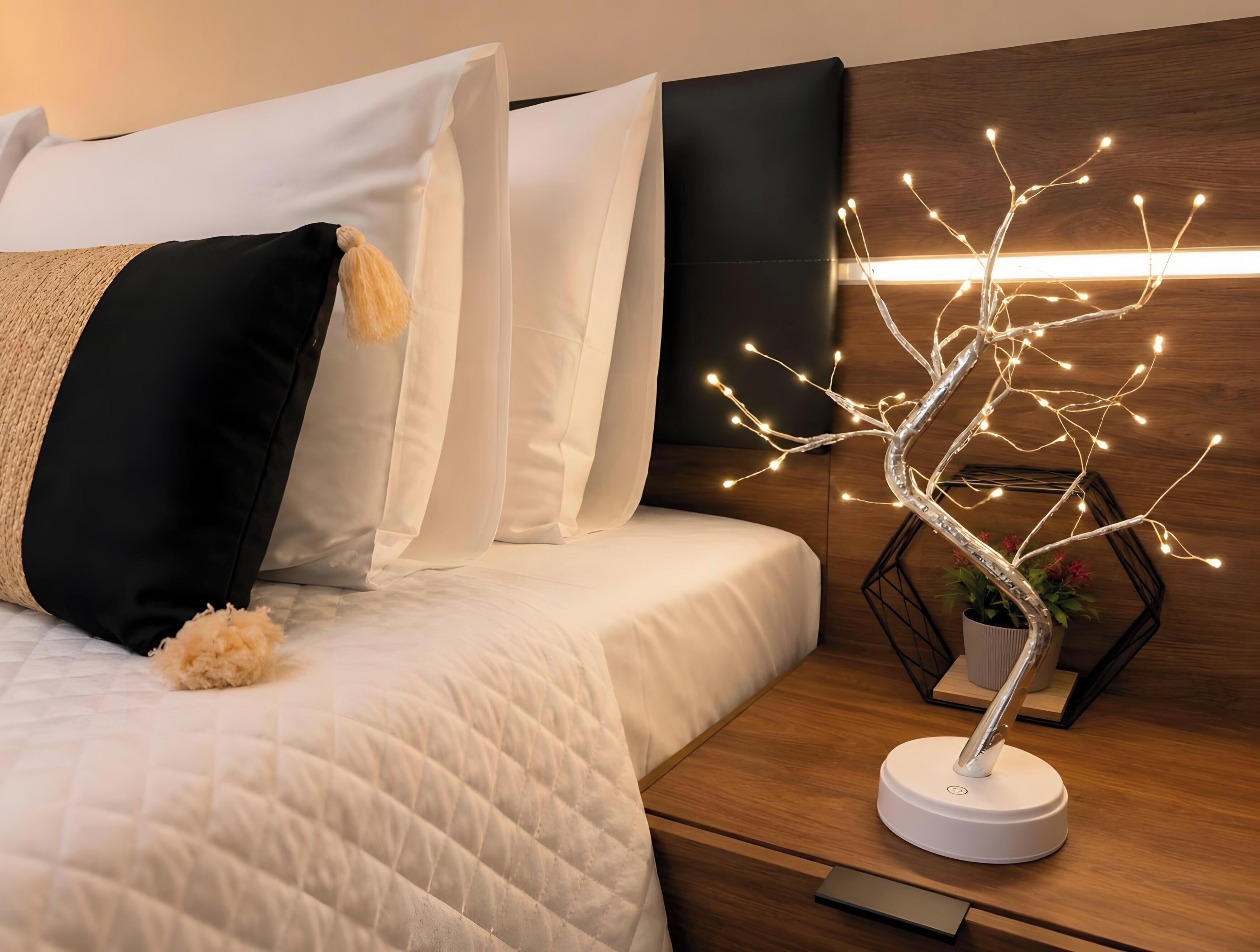 Un lit bien fait, avec une literie blanche et une guirlande lumineuse décorative en forme d’arbre.