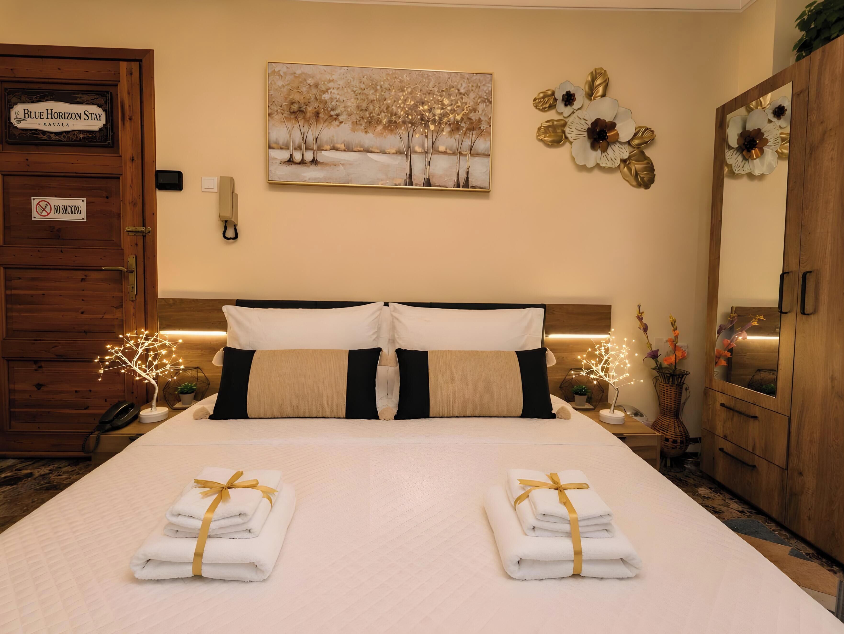 A hotel room with a bed, a 'No Smoking' sign, a painting of trees, and a wooden wardrobe.