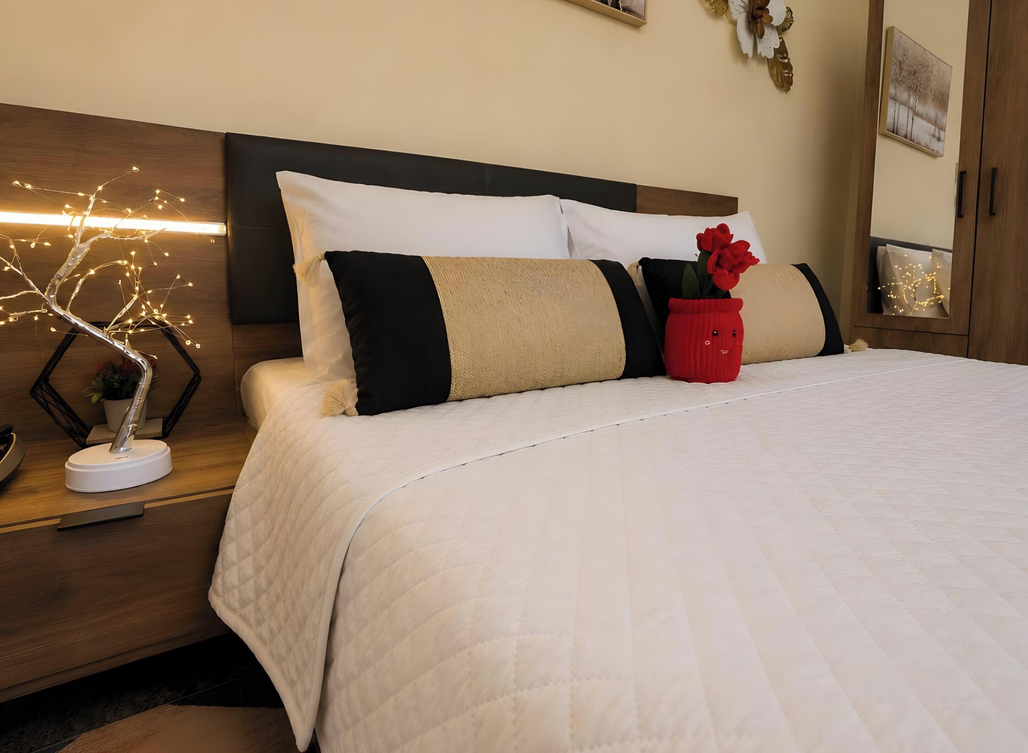 A neatly made bed with a white quilt, a wooden headboard, and a bedside table with a decorative tree light.