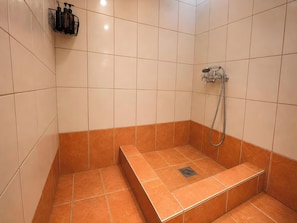 Un angolo doccia con pavimento e pareti piastrellate, un soffione e uno scaffale con articoli da toilette.