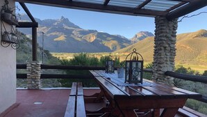 Mesa de piquenique de madeira com duas bancos, guarda-corpo de metal e vista para montanhas.
