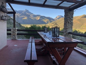 A wooden picnic table with two benches, a metal railing, and a view of mountains. - Chenin Blanc Cottage (Ladismith)