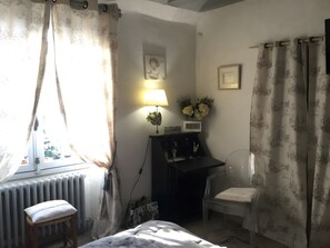 A bedroom with a bed, a desk with a lamp, a chair, and a radiator.