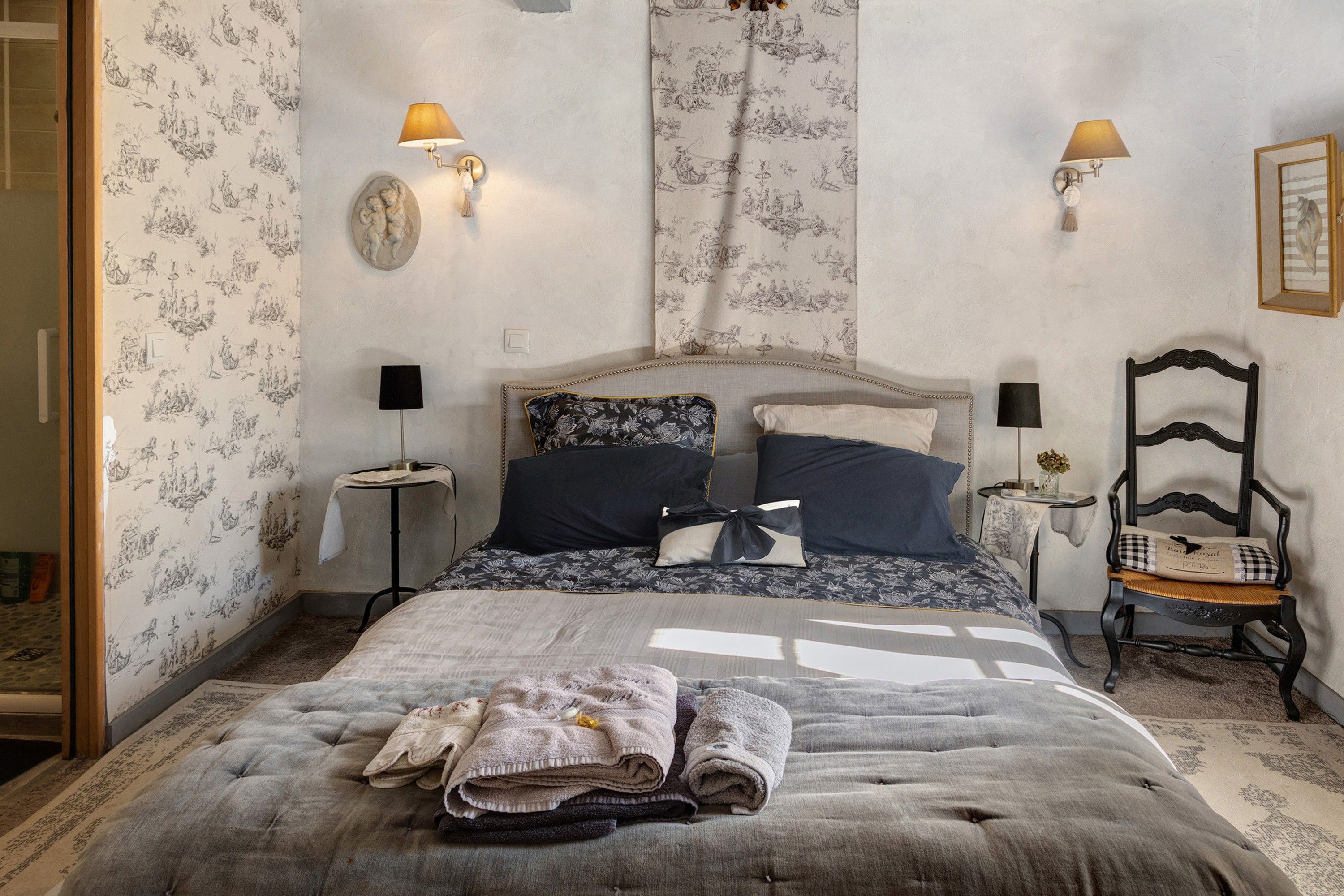 Een slaapkamer met een bed, twee wandlampen, een nachtkastje, een stoel en een decoratief kunstwerk aan de muur.