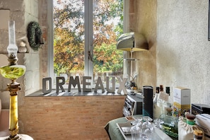 A cozy room with a large window, a decorative sign spelling 'ORMEAUX,' and a variety of bottles and glasses on the windowsill.