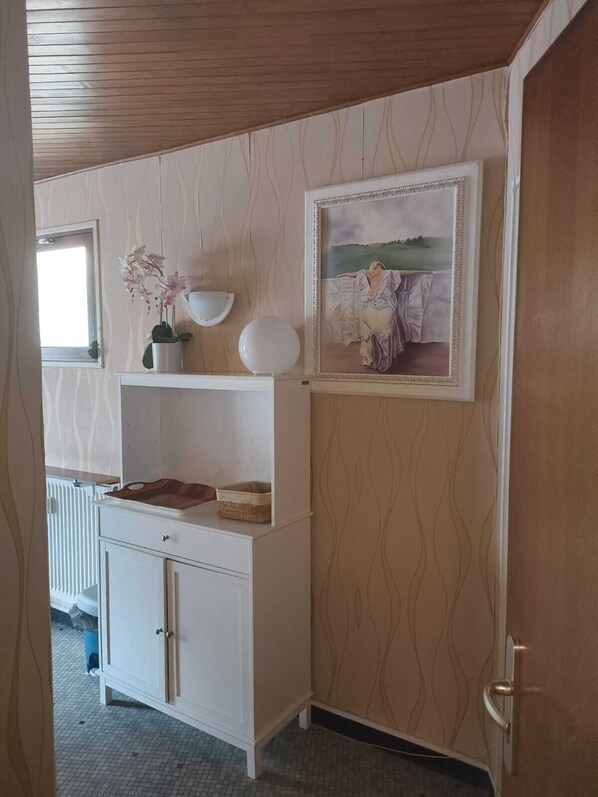 A room with a white cabinet, a framed painting, and a potted orchid.
