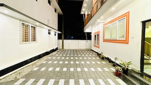 Un patio con piso a cuadros, plantas en macetas y un edificio blanco con detalles en naranja.
