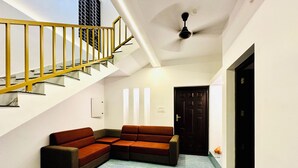 Un interior moderno con una escalera, un sofá modular, un ventilador de techo y una puerta.