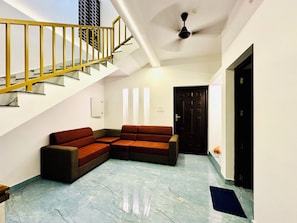 A modern interior with a staircase, a sectional sofa, a ceiling fan, and a door. - Varkala Escape Beach Resort (Varkala)