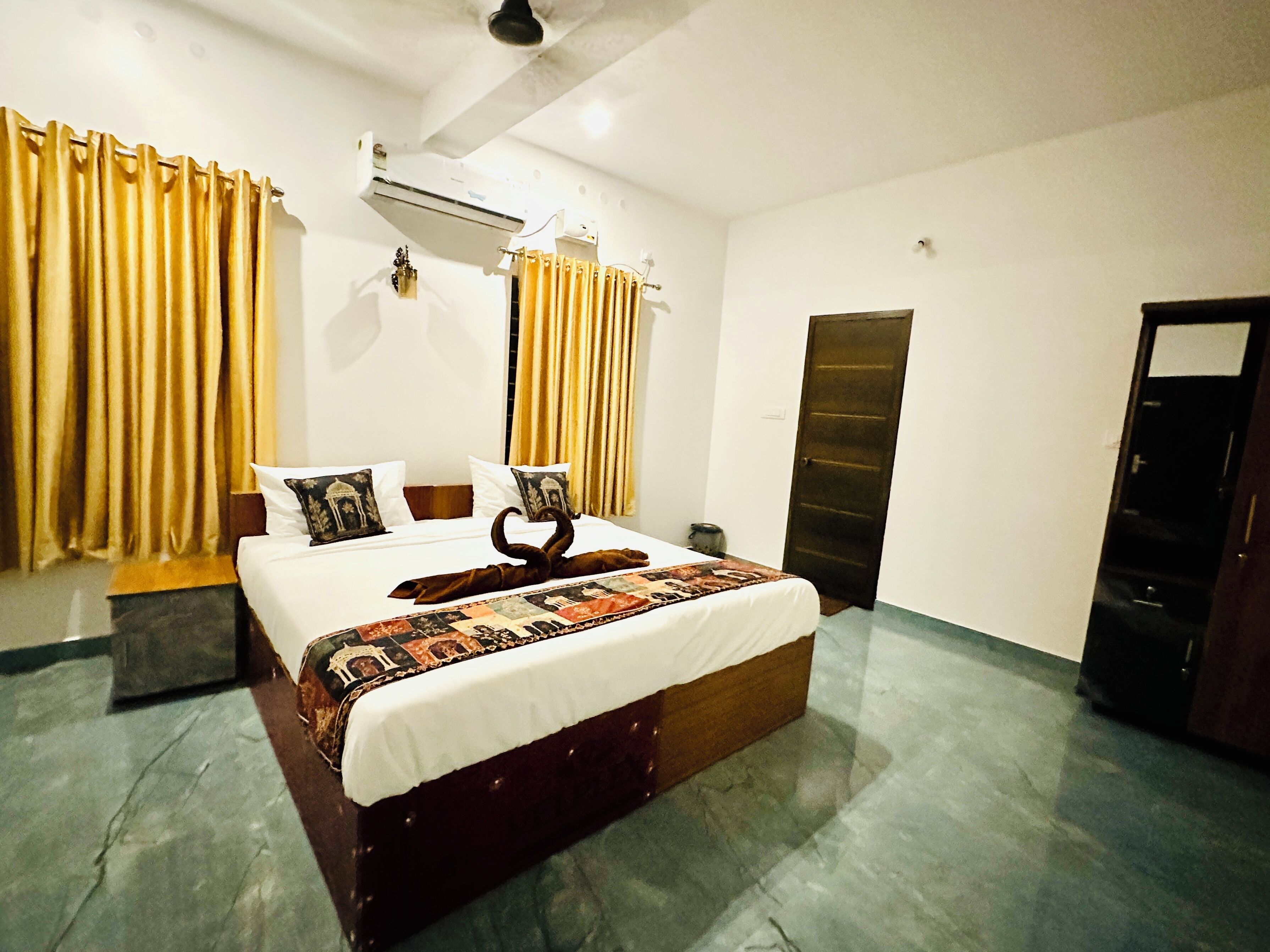 Habitación de hotel con cama, cortinas, aire acondicionado, una puerta y piso de baldosas.
