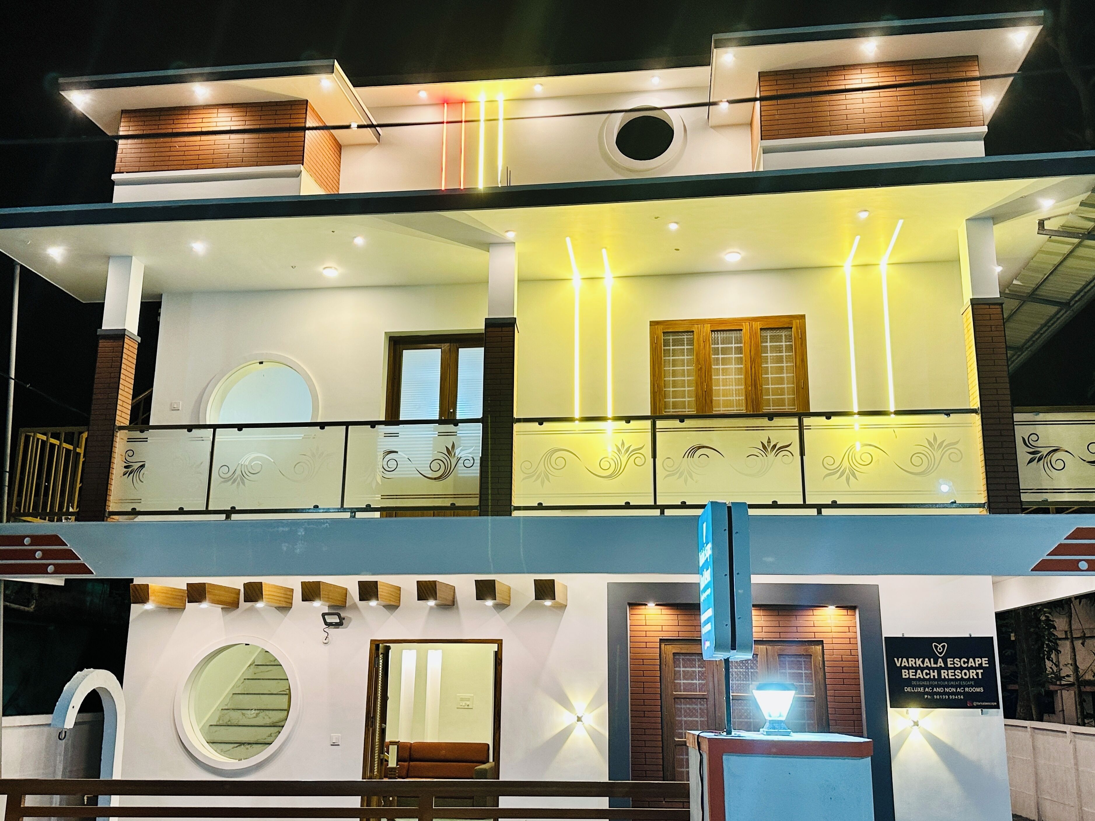 Een gebouw met twee verdiepingen, een balkon, een rond raam en een bordje met Varkala Escape Beach Resort erop.