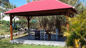 A covered outdoor seating area with a red roof, surrounded by greenery and a mountain backdrop. - Ti caz Lao Brasec, a Creole-style house in Bras Sec (Cilaos). (Cilaos)