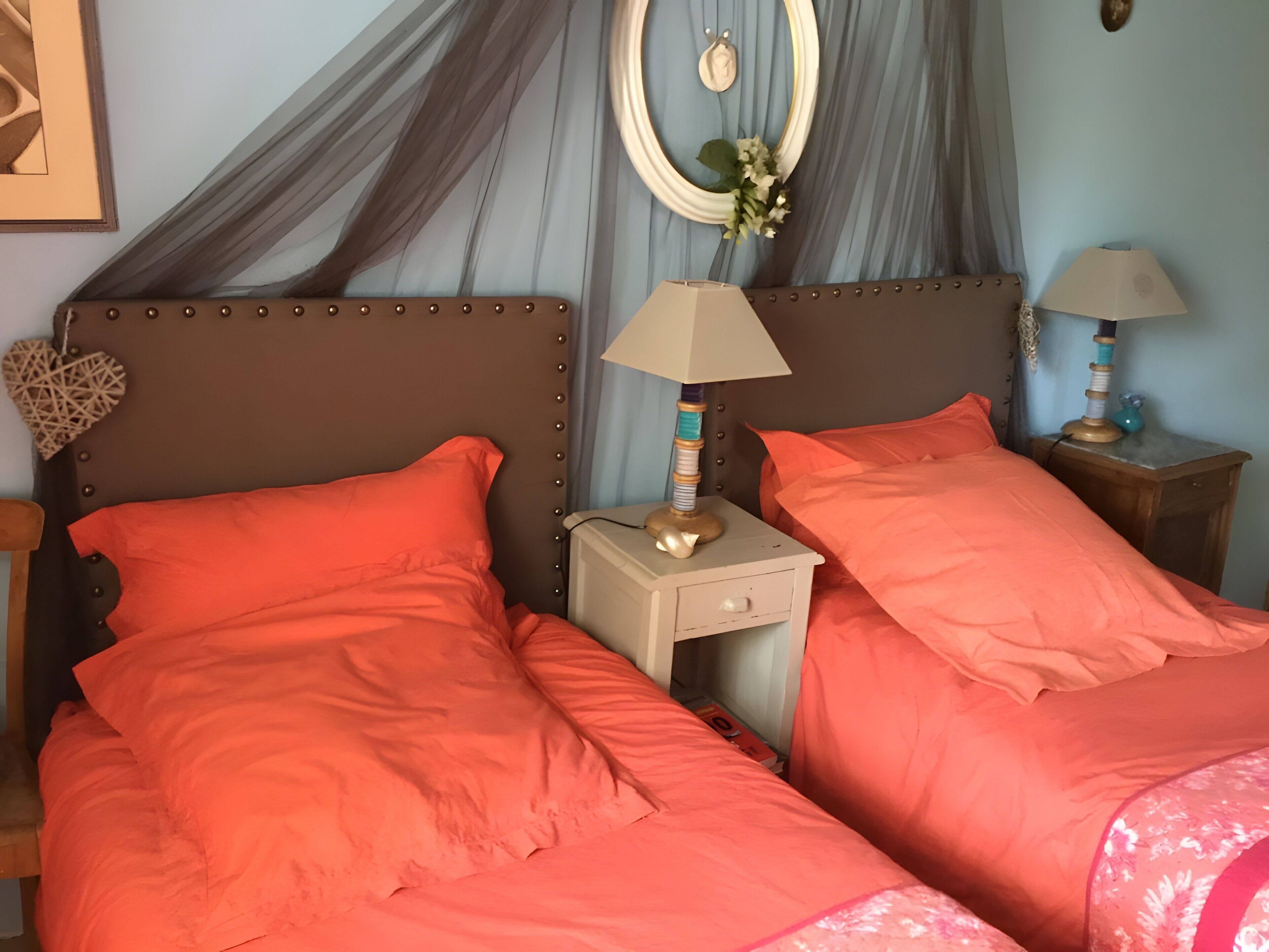Un dormitorio con dos camas, una mesita de noche con lámparas, un espejo decorativo y un adorno con forma de corazón.