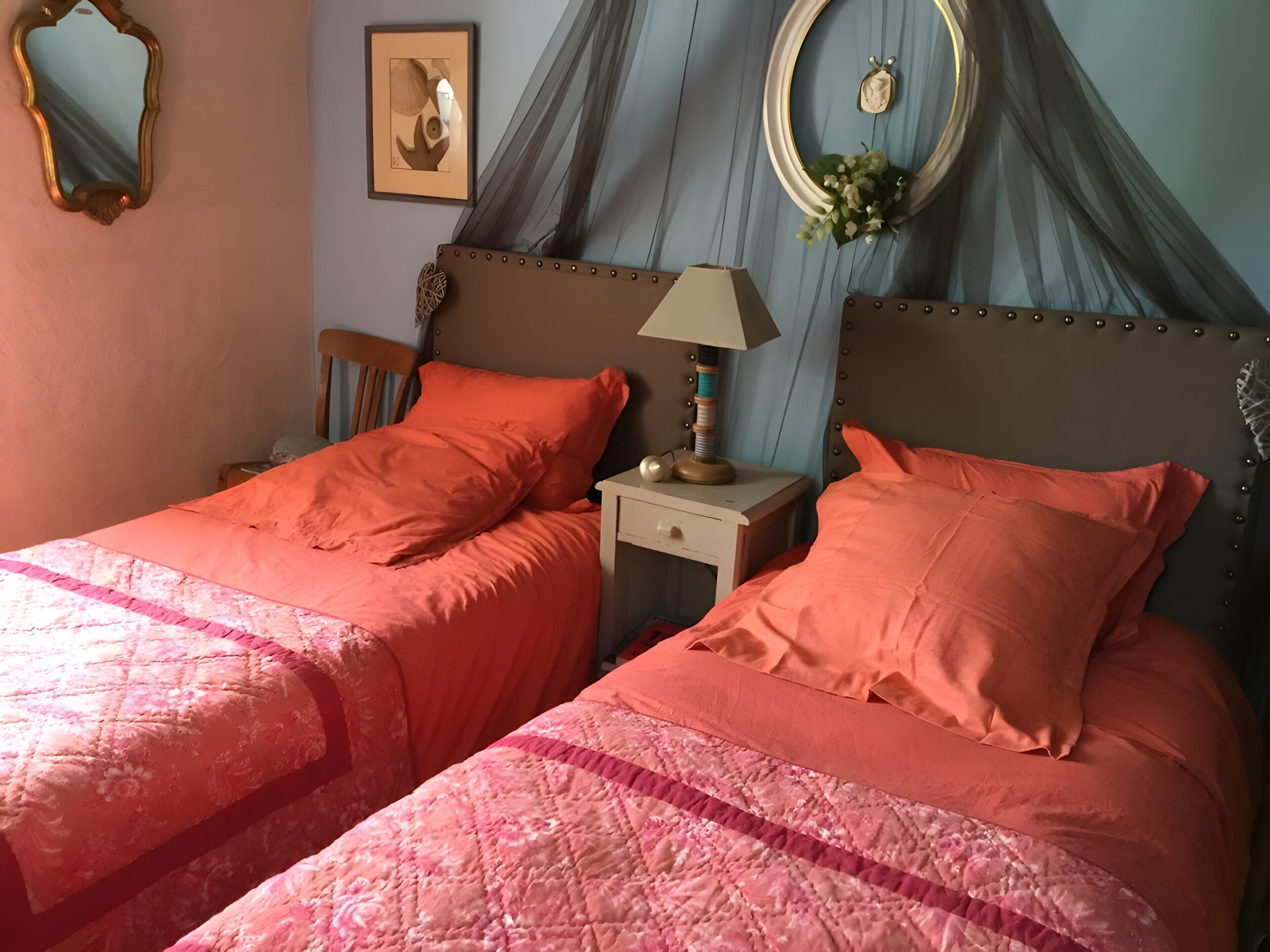 Een kamer met twee bedden, elk voorzien van passende kussens en een sprei. Er staat een nachtkastje met een lamp en een klein tafeltje met een decoratief object.