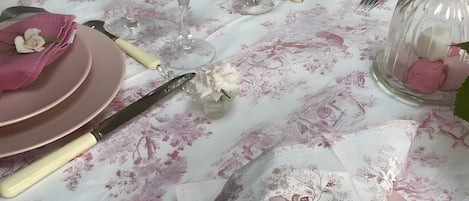 Una mesa dispuesta con platos rosas, copas transparentes y un mantel con motivos florales.