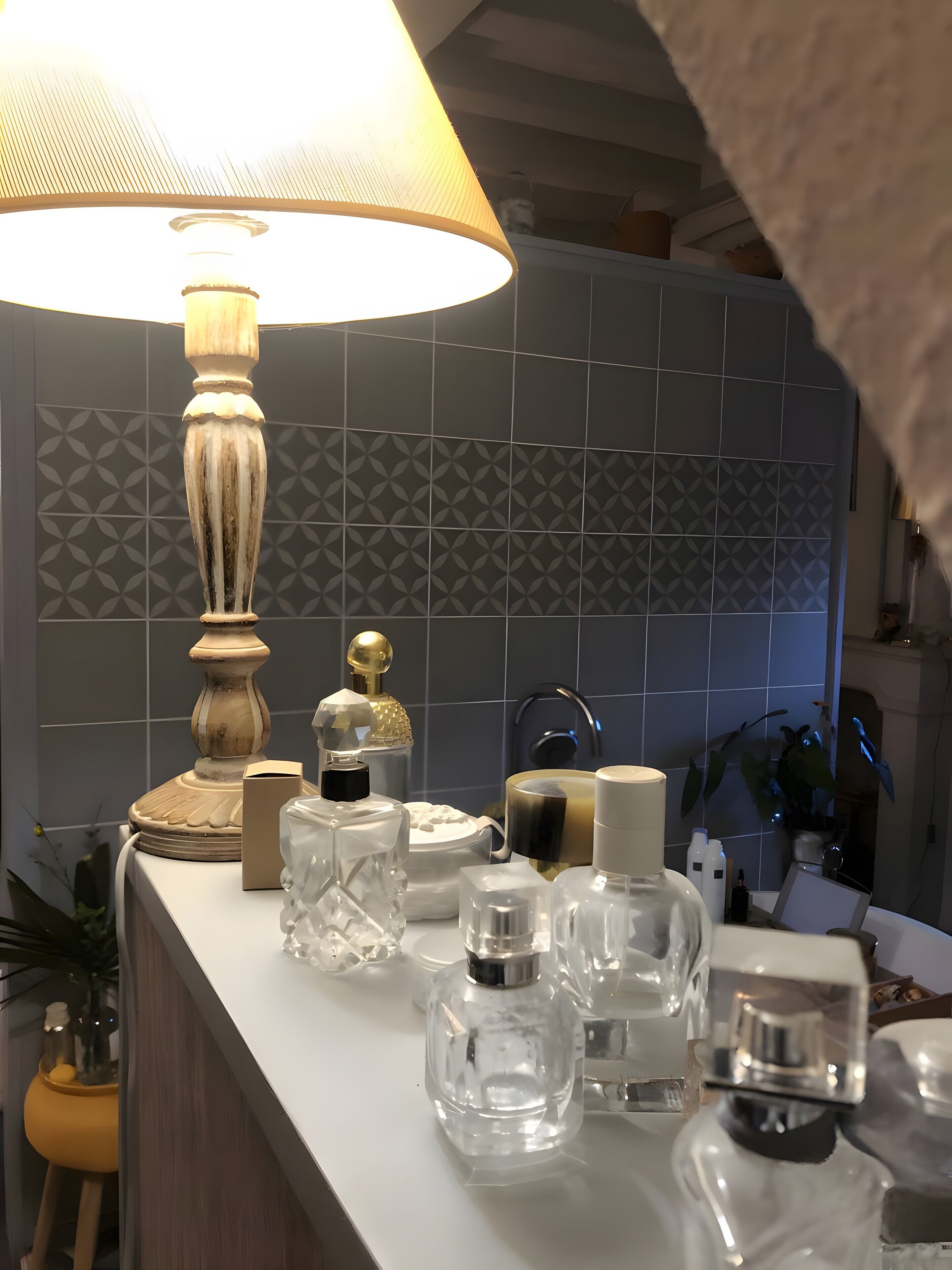 Une salle de bain avec un comptoir blanc, une lampe décorative et divers produits de toilette.