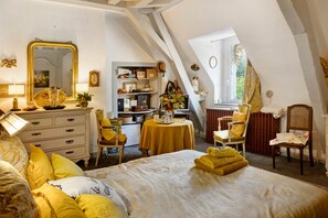 Une chambre à coucher avec un grand lit, une commode, une coiffeuse avec un miroir, une petite table avec un vase et une bibliothèque.
