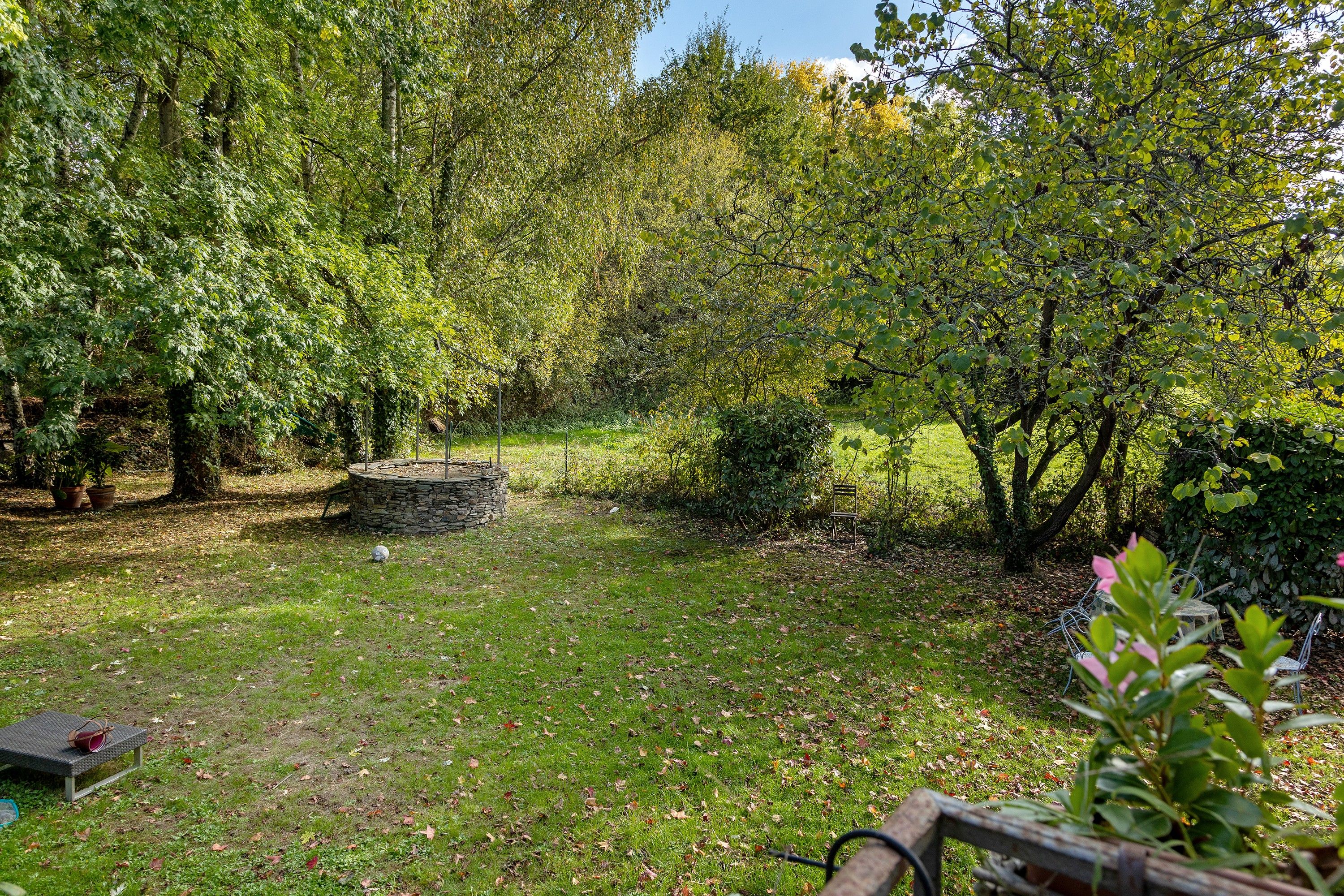 Een tuin met een stenen constructie, een bankje en verschillende bomen.