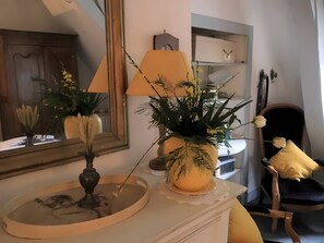 A room with a mirror, a lamp, a chair, and a potted plant on a dresser.