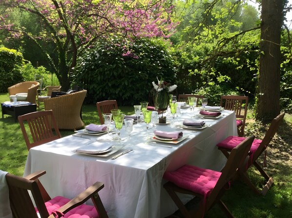 An outdoor dining area with a table set for a meal, surrounded by chairs with cushions.
