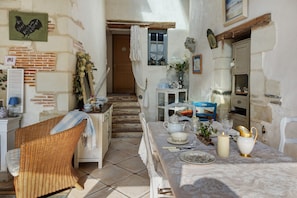 Un coin repas rustique avec une table dressée pour deux personnes, une chaise en osier et un escalier menant à une porte.