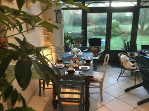 Un comedor con una mesa preparada para cuatro, sillas, un oso de peluche y vista a un jardín a través de un ventanal.