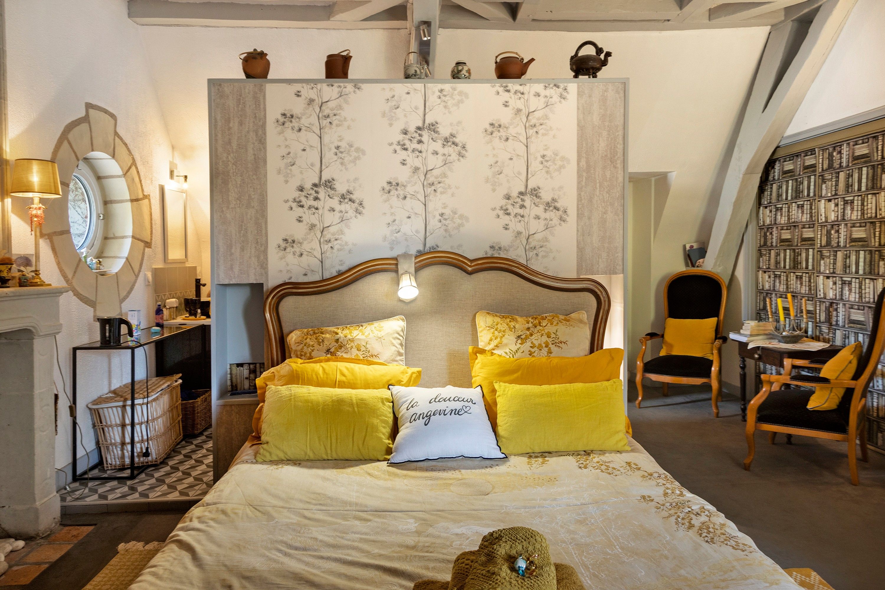 Ein Schlafzimmer mit einem großen Bett, einem Nachttisch, einem Sessel, einem Bücherregal und einem Spiegel.