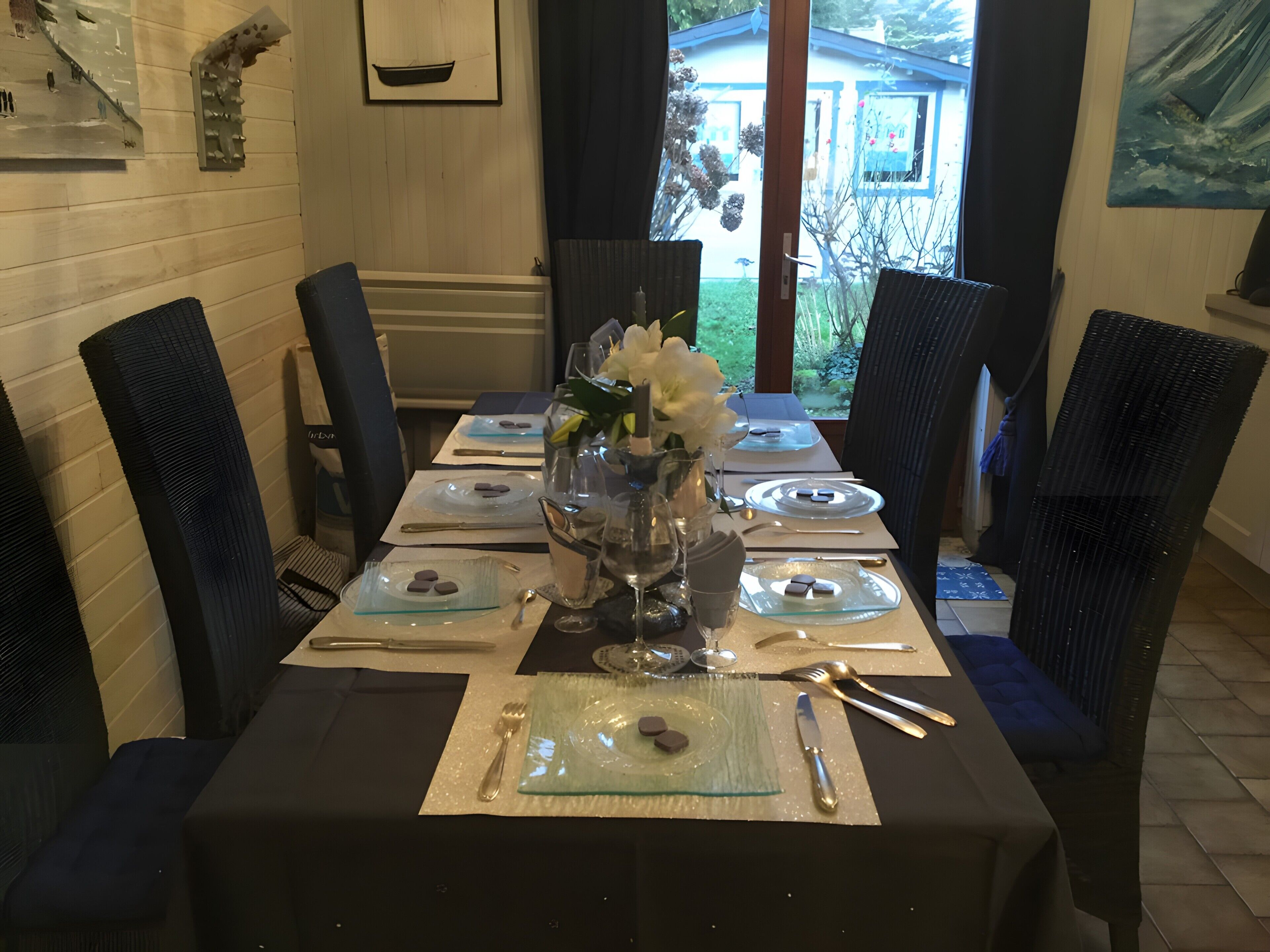 A dining table set for four with a vase of flowers, plates, cutlery, and a glass of water.
