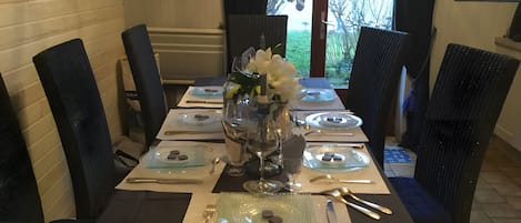 A dining table set for four with a vase of flowers, plates, cutlery, and a glass of water.