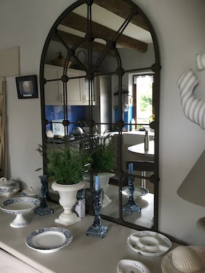 A kitchen with a large mirror reflecting the room, a dining table with chairs, and various kitchenware and decorative items. - Éole – Family House with Shared Terrace, Private Garden, and Wi-Fi (Cancale)