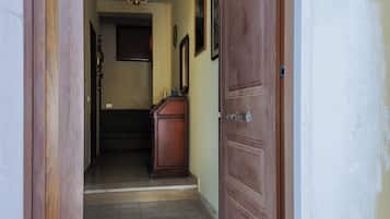 Un couloir avec une porte en bois, un canapé de couleur sombre et un luminaire fixé au mur.
