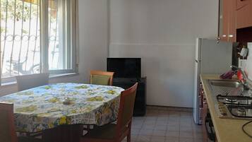 A compact kitchen with a dining table and chairs, a television, and a gas stove.