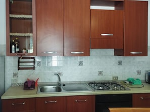 A kitchen with wooden cabinets, a stainless steel sink, a gas stove, and a tiled backsplash. - Casa Vacanza da Nicola 2 (Cavaliere)