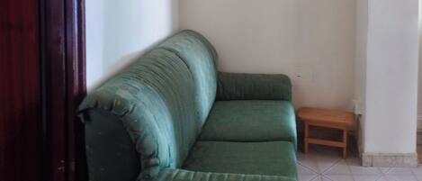 Un sofá verde en una habitación con piso de baldosas y un taburete de madera.