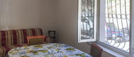 Una habitación con una mesa redonda cubierta con un mantel floral, un sofá a rayas y una ventana con una reja de metal.