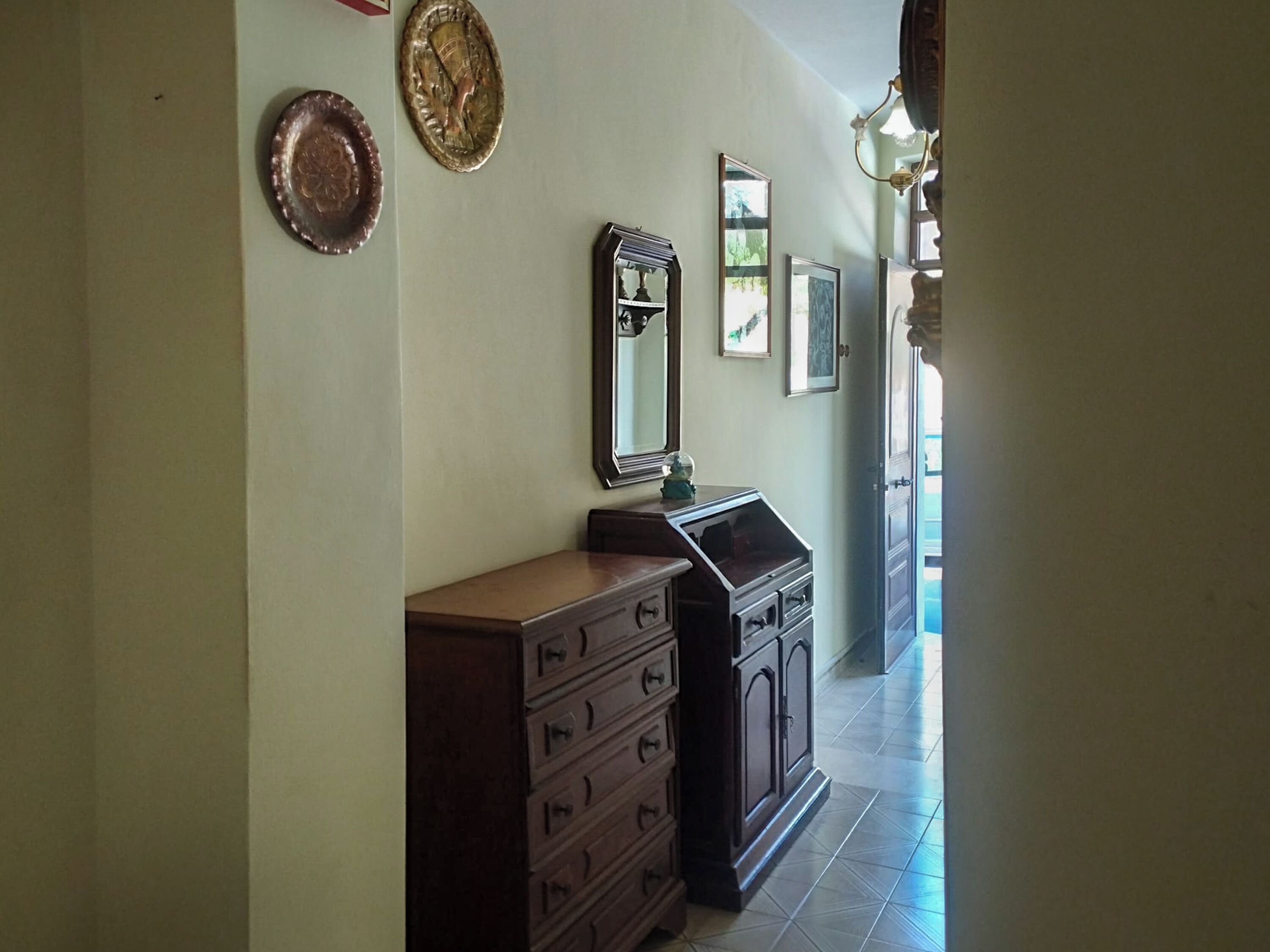 Un couloir avec une commode en bois et un miroir au mur.