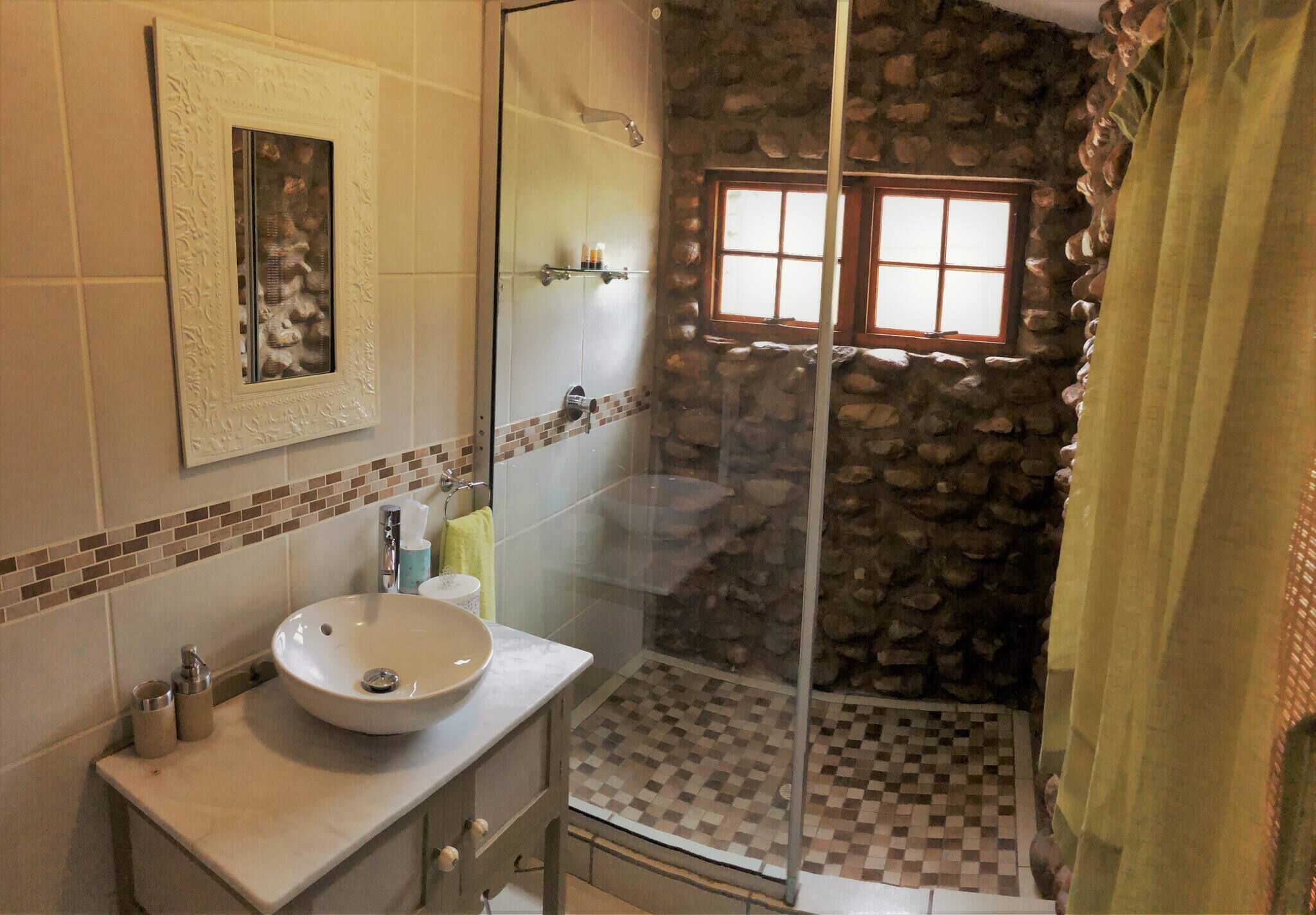 A bathroom with a stone shower enclosure, a sink with a mirror, and a window.