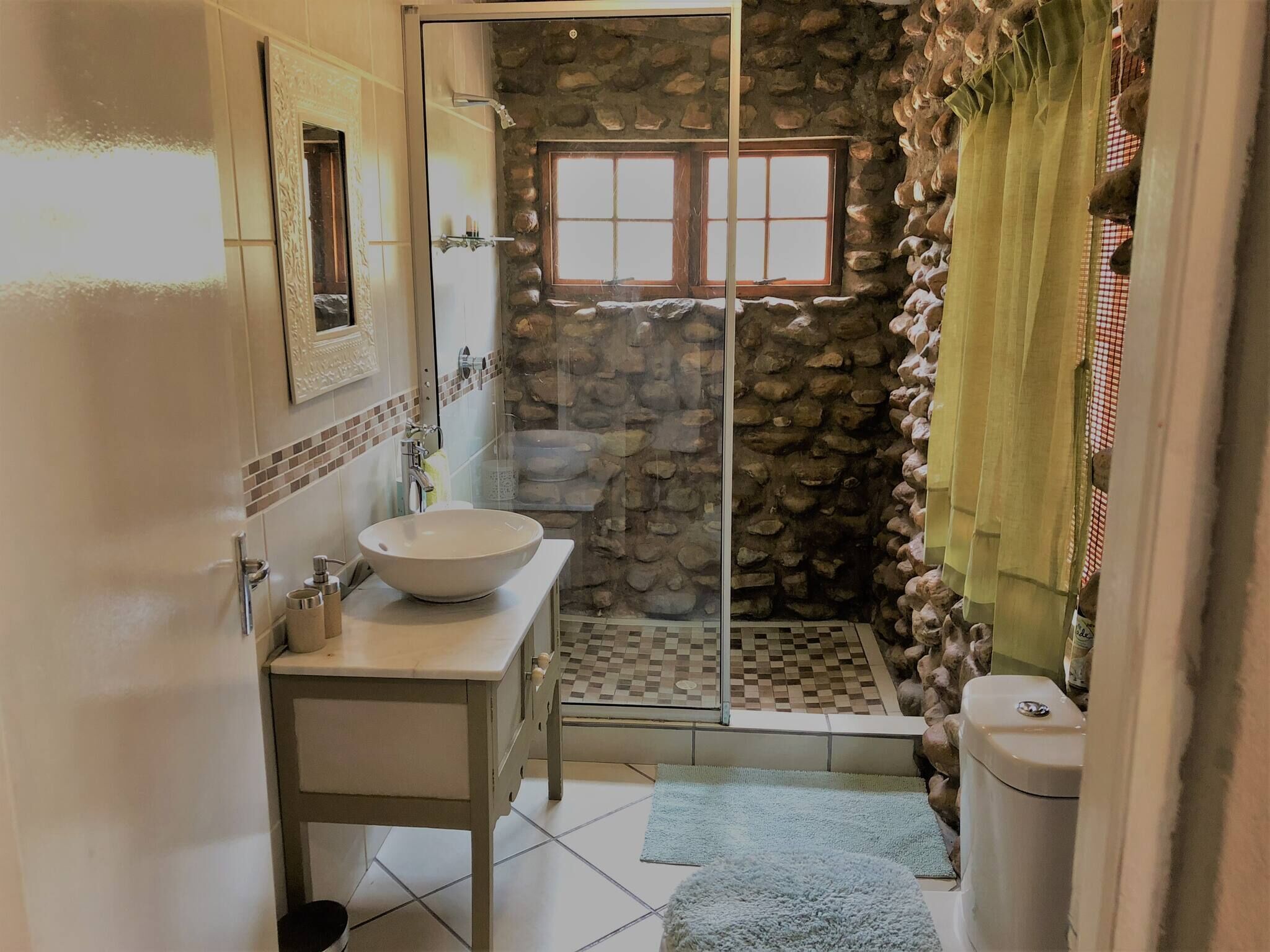 Un bagno con parete in pietra, cabina doccia in vetro, lavandino bianco e water.