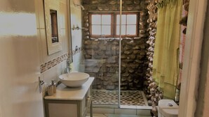 A bathroom with a stone wall, a glass shower enclosure, a white sink, and a toilet. - Spacious Farmhouse Rental in Ladismith With Stunning Views (Ladismith)