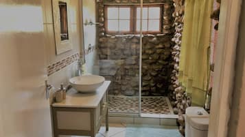 Un bagno con parete in pietra, cabina doccia in vetro, lavandino bianco e water.