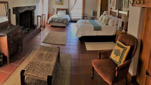 A traditional room with a fireplace, two beds, a wooden chair, and a chandelier.