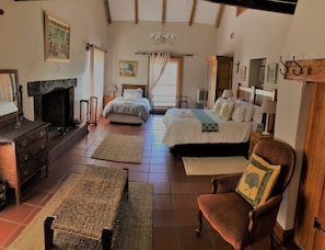 A traditional room with a fireplace, two beds, a wooden chair, and a chandelier.