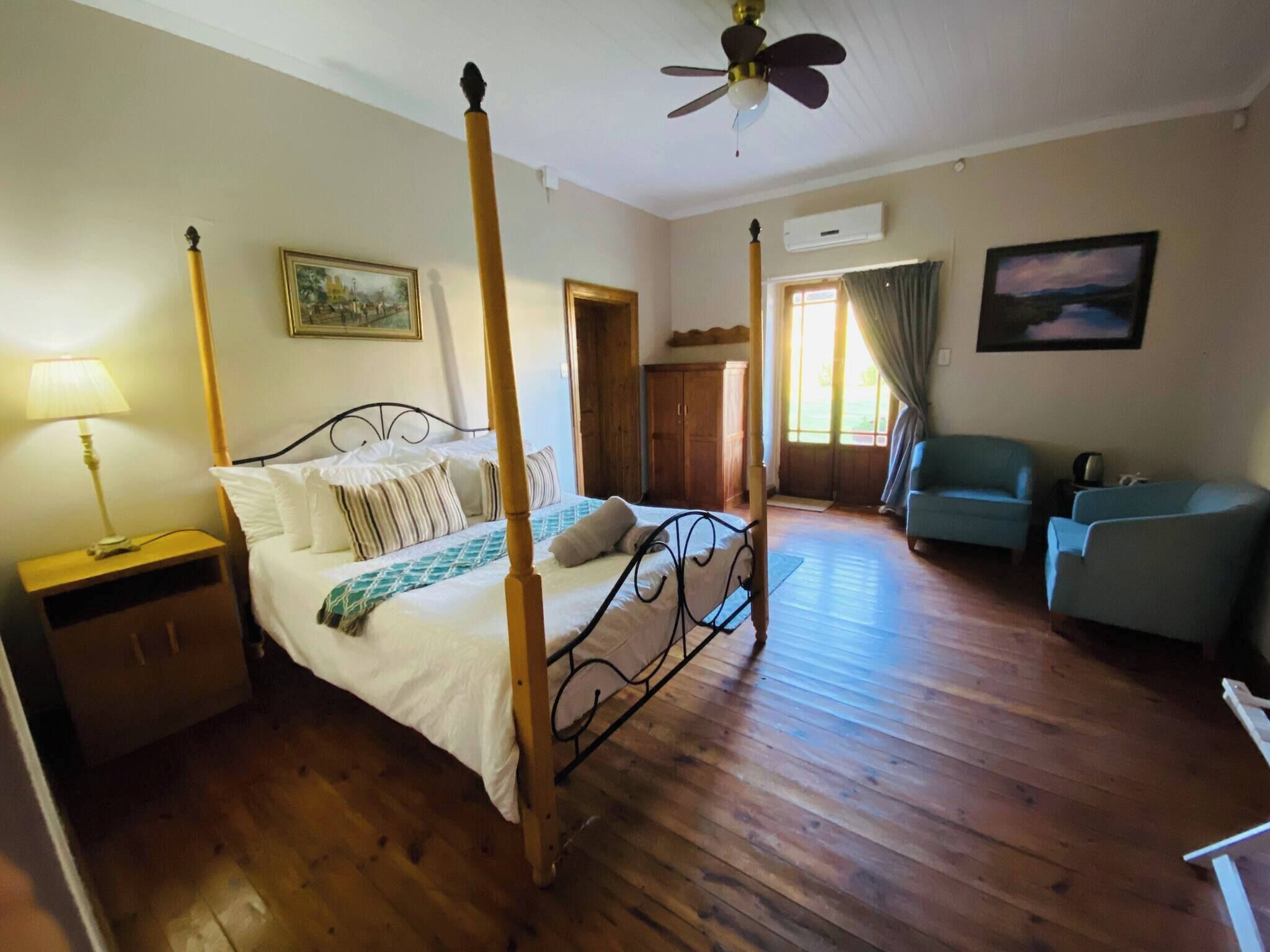 Un letto a baldacchino con struttura in legno, un comodino, una lampada, un quadro appeso al muro, un armadio, una sedia e una ventola a soffitto.