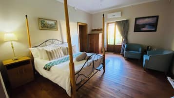 Un letto a baldacchino con struttura in legno, un comodino, una lampada, un quadro appeso al muro, un armadio, una sedia e una ventola a soffitto.