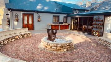 A courtyard with a central fire pit, surrounded by stone walls and a brick floor.