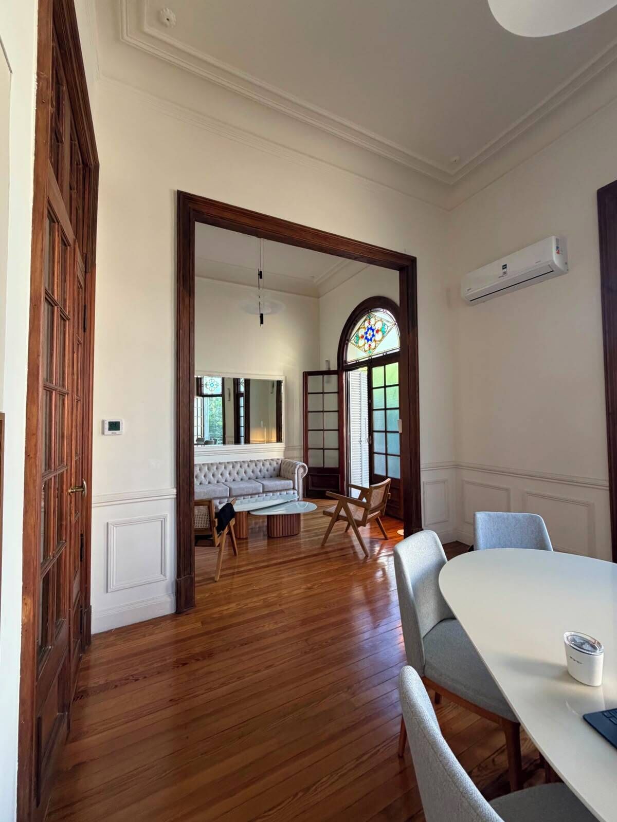 Una habitación con techo blanco, suelo de madera, un sofá blanco, una mesa redonda y una silla.